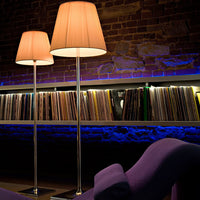 Modern floor lamps with soft peach shades, sleek silver bases, and a vibrant purple chair against a textured brick wall.