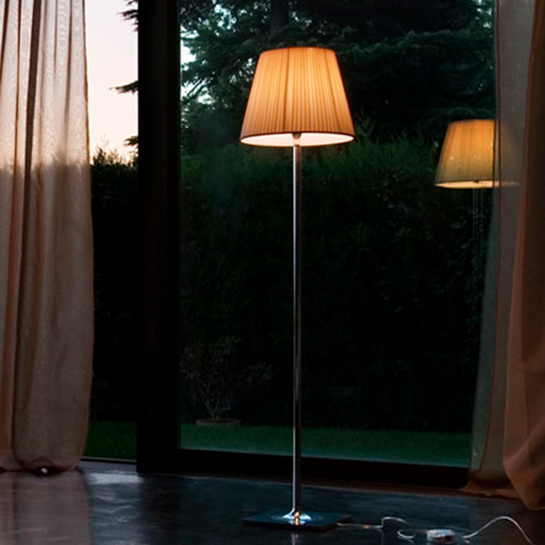 Tall floor lamp with a soft beige shade and sleek silver stand, illuminating a modern indoor setting.