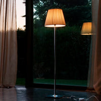 Tall floor lamp with a soft beige shade and sleek silver stand, illuminating a modern indoor setting.