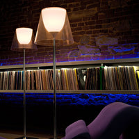 Modern floor lamps with soft white shades and sleek silver bases, set against a cozy brick backdrop with ambient blue lighting.