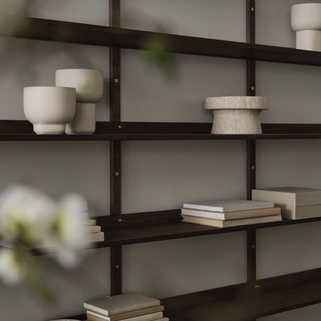 Dark wood shelves with neutral ceramic bowls and stacks of white and beige books against a light gray background.