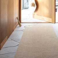 Beige indoor runner rug on stone flooring, enhancing warm, neutral tones in a bright entryway.