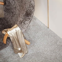 Soft gray plush chair with a luxurious beige satin ribbon draped over a light gray textured floor.