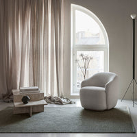 Cozy white armchair on textured green rug, surrounded by soft beige curtains and a minimalist decor.