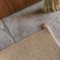 Textured beige rug corner on smooth gray stone floor, accented by light wood and natural brush.