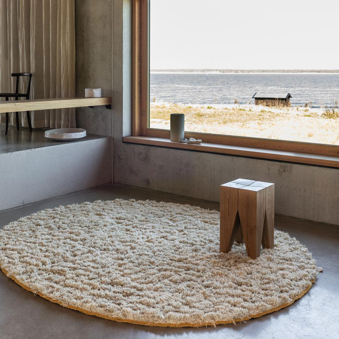 Round, fluffy cream rug with a beige border, perfect for adding warmth and texture to any room.
