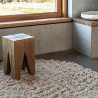 Natural wood stool with geometric design, set on a textured cream-colored shag rug in a modern interior.