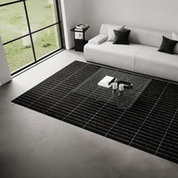 Black and white grid-patterned rug on a modern floor, complementing a light gray sofa and glass coffee table.