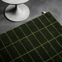 Green plaid rug with contrasting light green grid pattern on dark green background, showcased on a gray surface.