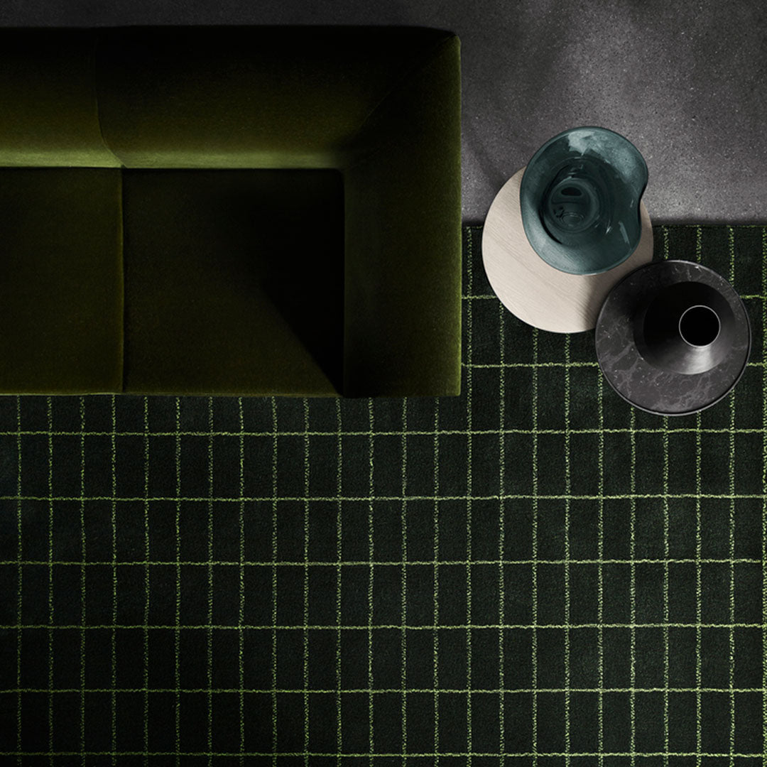 Black and green grid-patterned rug with a modern design, complementing a dark green couch and stylish decor.