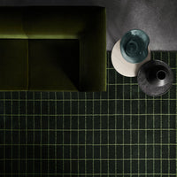 Black and green grid-patterned rug with a modern design, complementing a dark green couch and stylish decor.