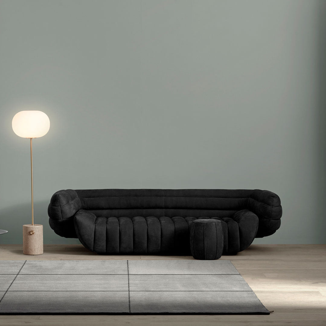 Black plush sofa with distinctive padded design, set against a soft green wall and neutral-toned floor.