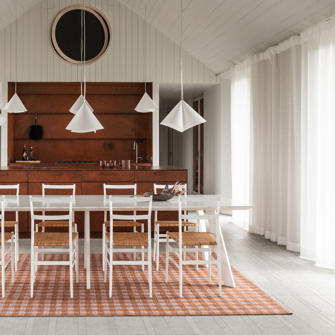 Modern dining room featuring a white table and chairs on a textured orange checkered rug, accented by minimalist pendant lights.