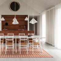 Modern dining room featuring a white table and chairs on a textured orange checkered rug, accented by minimalist pendant lights.