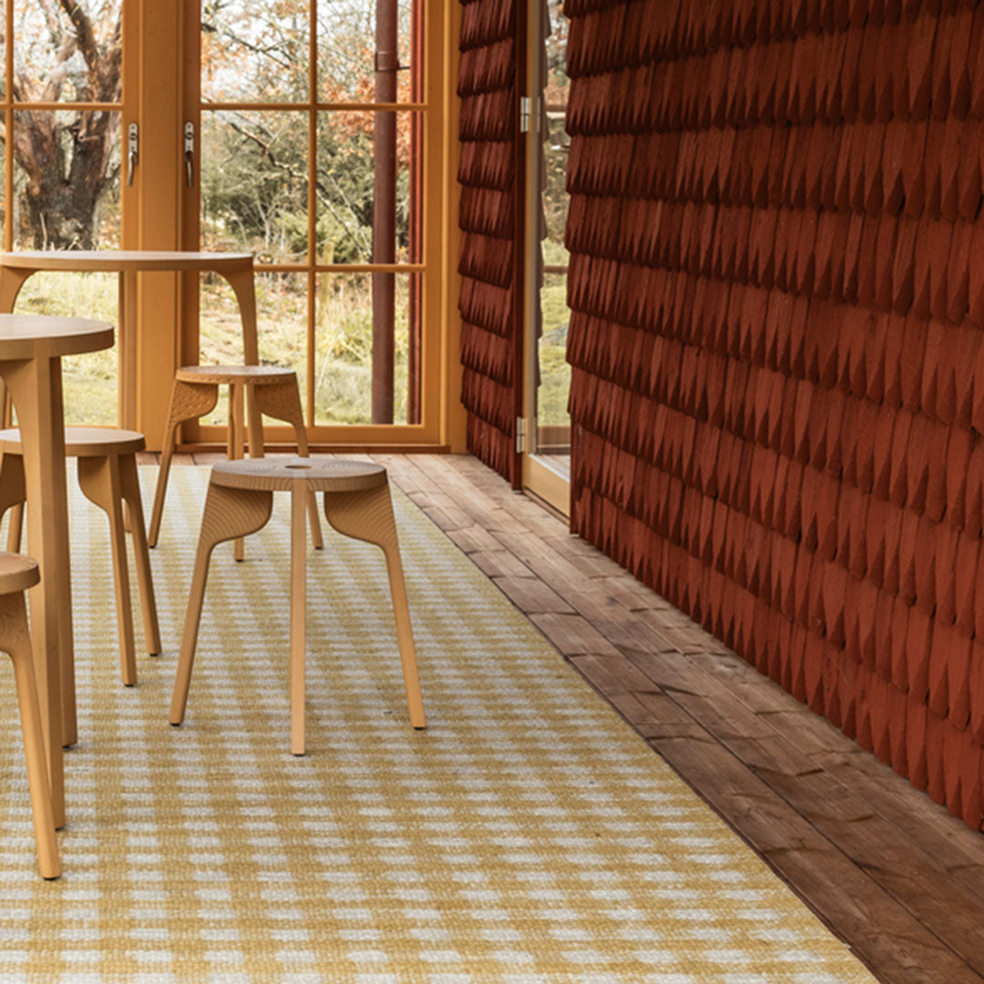 "Beige and yellow checkered rug with warm, earthy red wooden wall in a modern interior setting."
