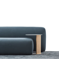 Modern dark blue upholstered sofa with smooth lines and a wooden side table on a soft, neutral rug.