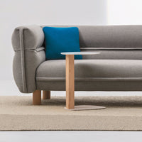 Gray sofa with a teal throw pillow and a minimalist wood accent table on a light beige rug.