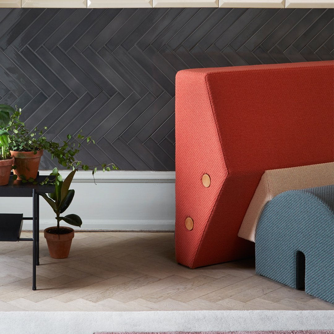 Red and blue upholstered furniture against a herringbone-patterned dark wall, with vibrant greenery accents.