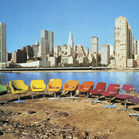 Row of colorful chairs in vibrant yellow, orange, purple, and green against a city skyline backdrop.