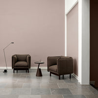 Brown upholstered armchairs against a soft pink wall, with a sleek gray tile floor and a minimalistic side table.