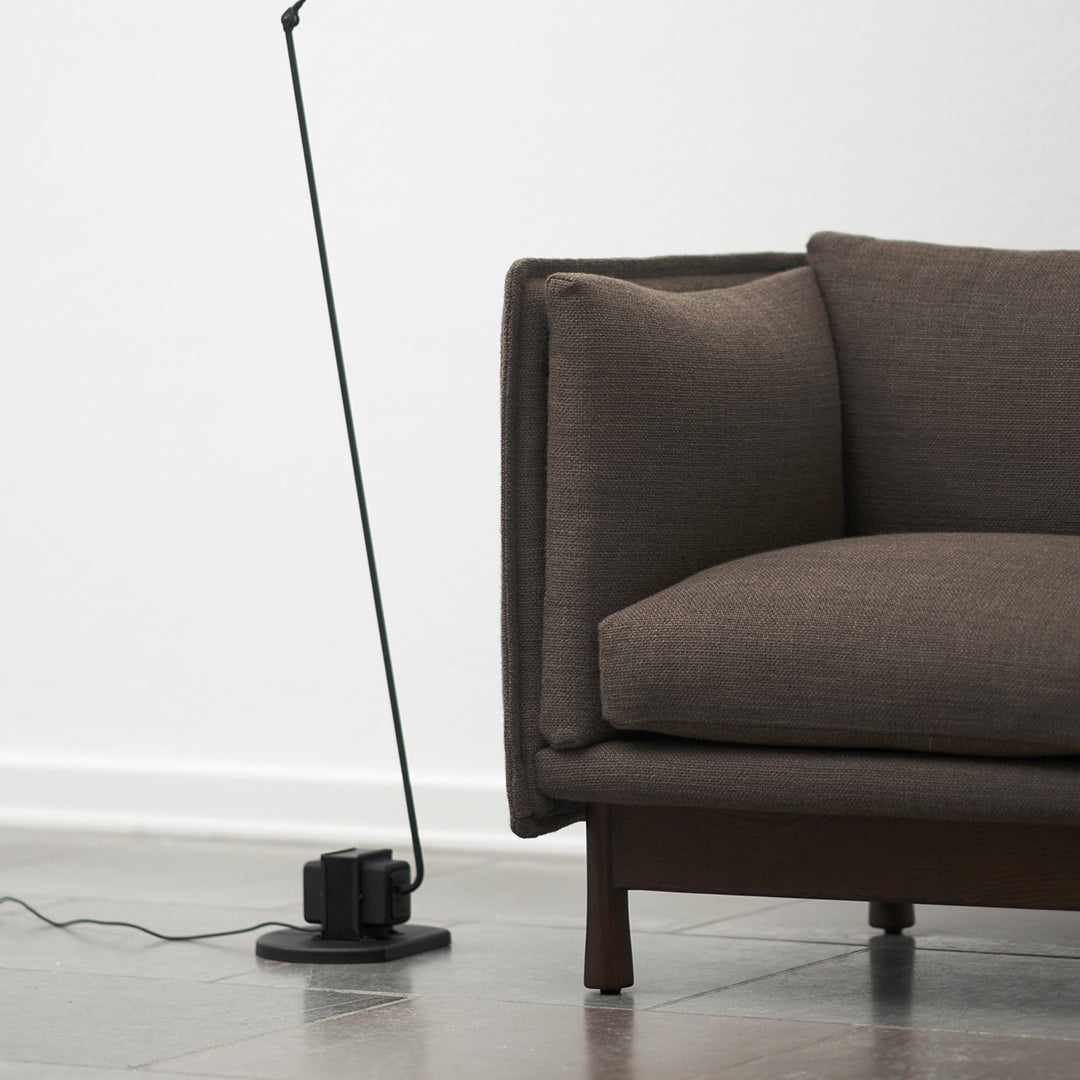 "Brown textured couch with clean lines beside a sleek black floor lamp on a light-colored tile floor."