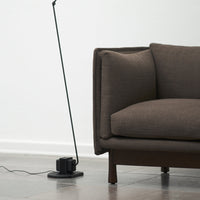 "Brown textured couch with clean lines beside a sleek black floor lamp on a light-colored tile floor."