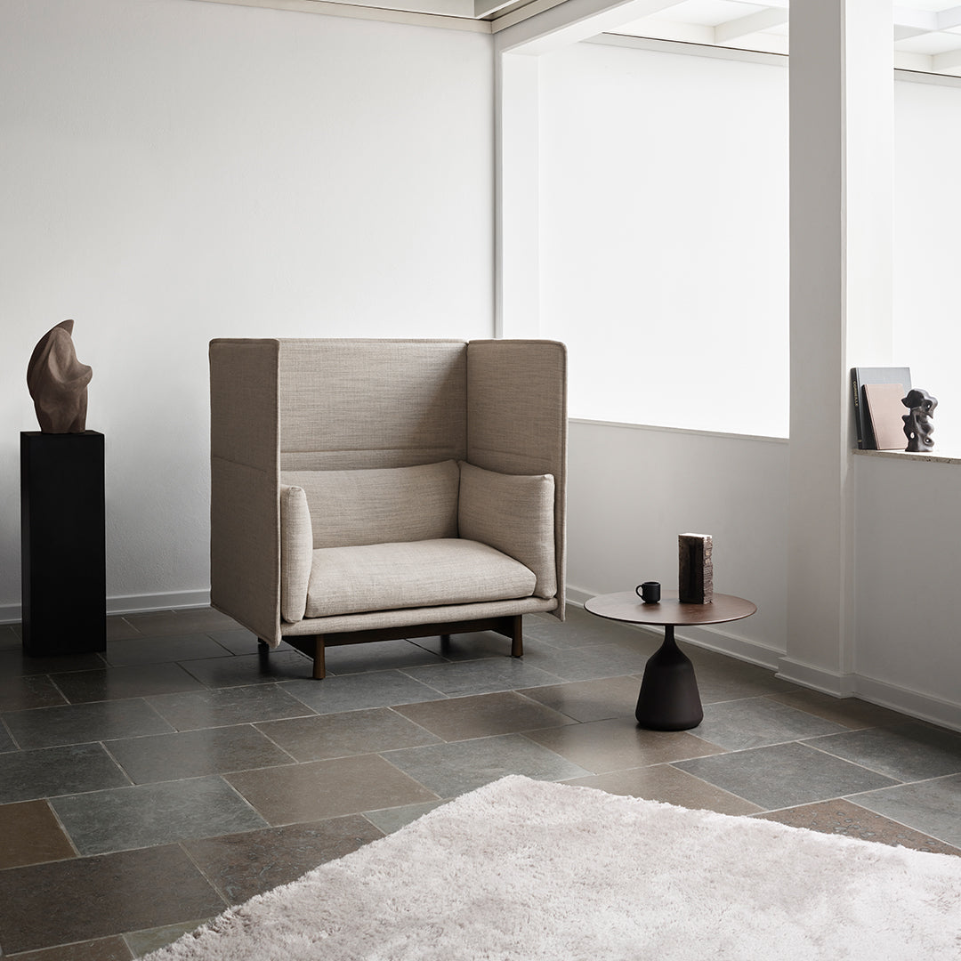 Modern beige armchair with clean lines, set against a minimalist white and gray backdrop, featuring subtle texture.