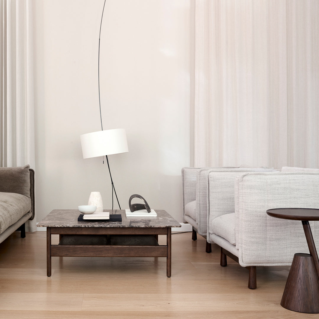 Neutral tones with soft gray armchairs, a dark wood coffee table, and light curtains create a modern, serene living space.