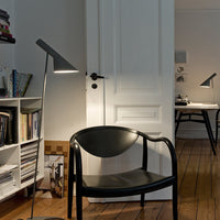 Black modern chair with a circular seat and sleek gray lamp, set against a neutral backdrop and wooden floor.