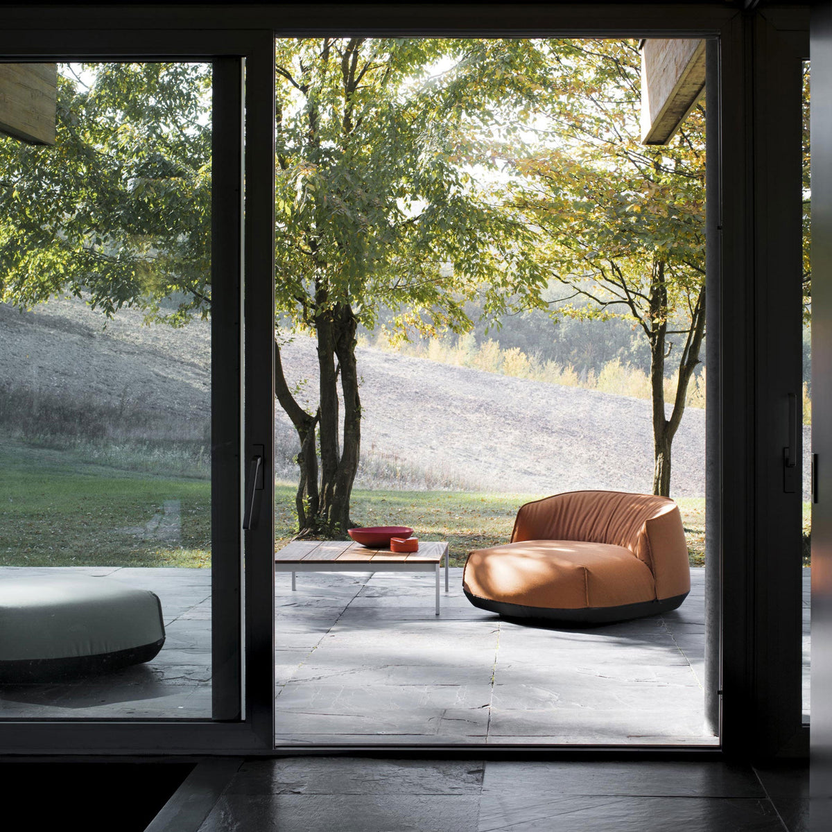 "Modern outdoor setting featuring an orange bean bag chair, gray patio table, and vibrant greenery."