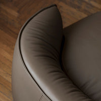 Brown leather chair with a smooth, curved design and subtle stitching details. Elegant and modern aesthetic.