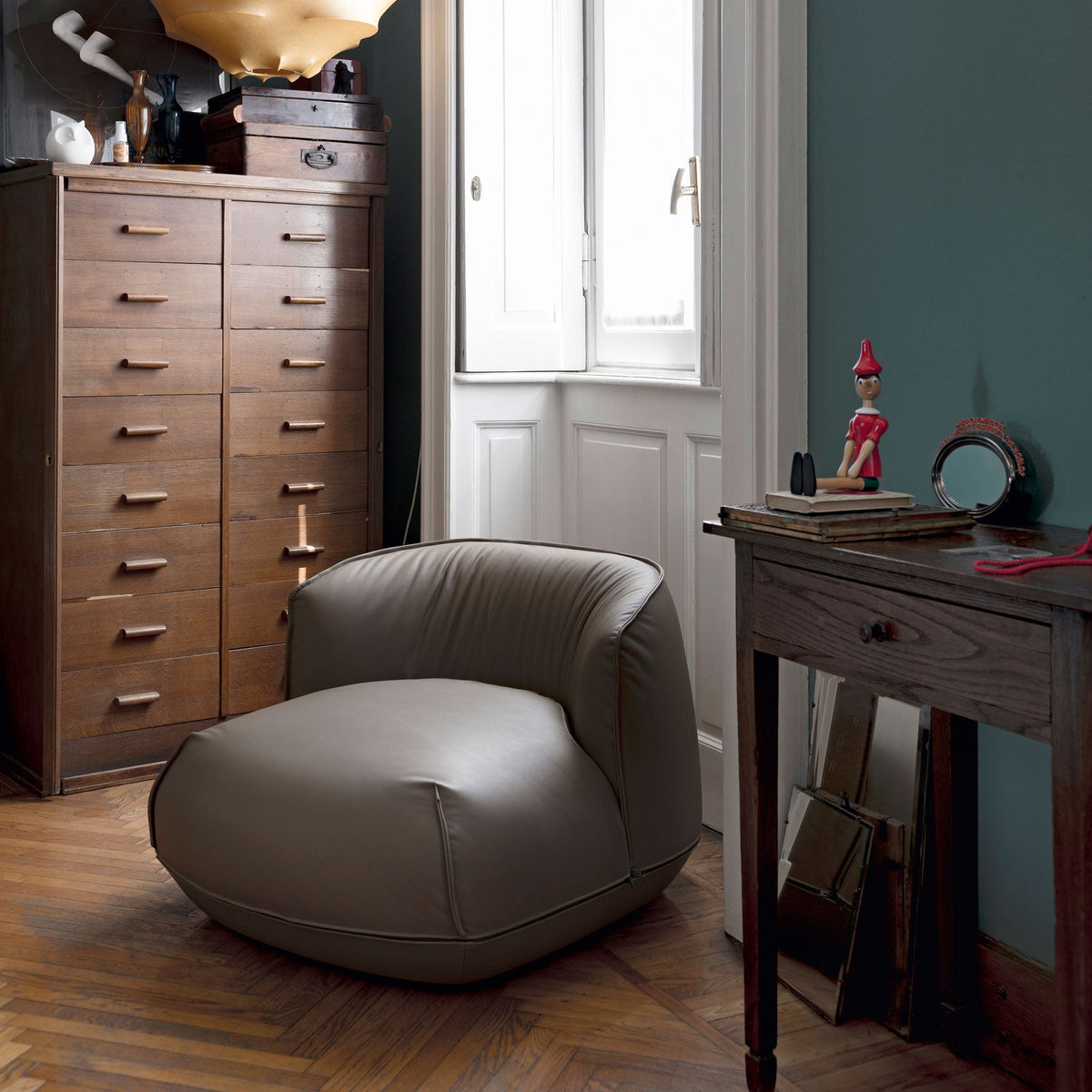 "Light beige round armchair with smooth leather texture against a blue wall and wooden furniture."