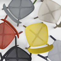 Colorful chairs in red, yellow, gray, black, green, and beige with unique perforated patterns, arranged creatively.