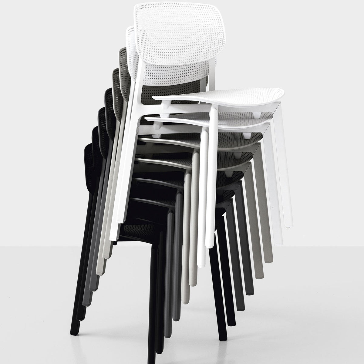 Stacked chairs in white, gray, and black featuring modern perforated patterns against a minimalist background.