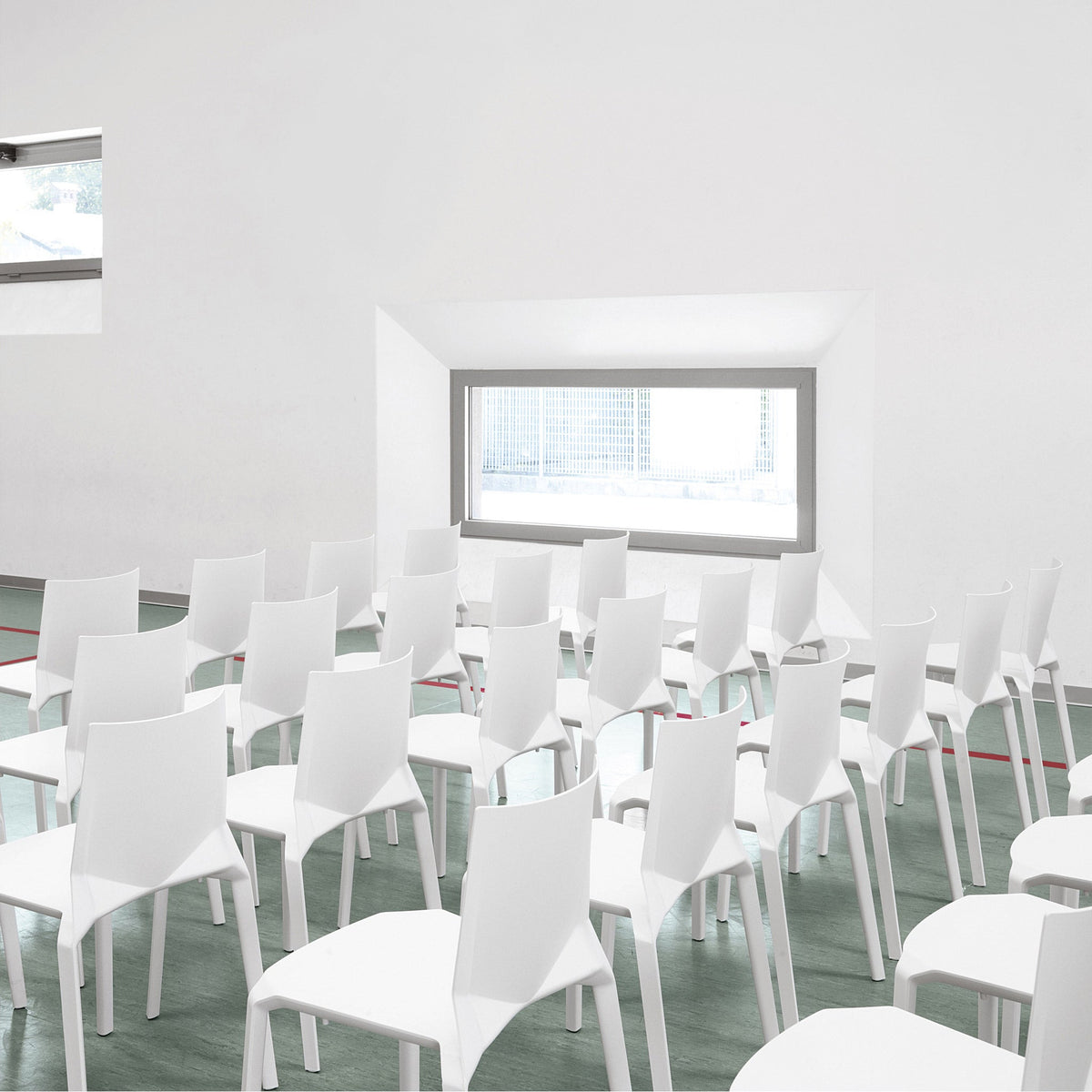 White modern chairs arranged in a bright space with green flooring and soft light streaming through a window.