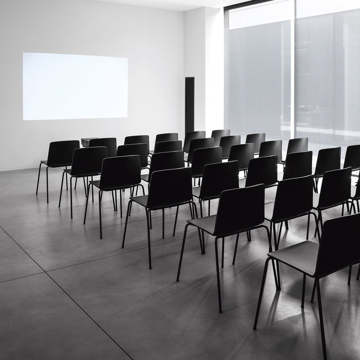Minimalist black chairs arranged in a modern, light-filled space with concrete flooring and white walls.