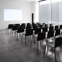 Minimalist black chairs arranged in a modern, light-filled space with concrete flooring and white walls.