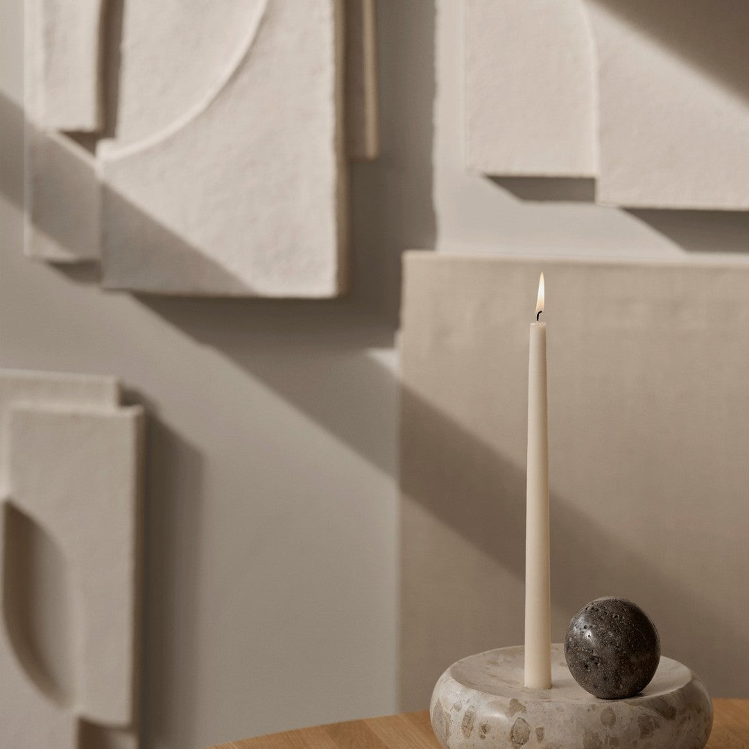 Beige and neutral decorative wall panels with a minimalist candle holder and round stone accent on a wooden table.