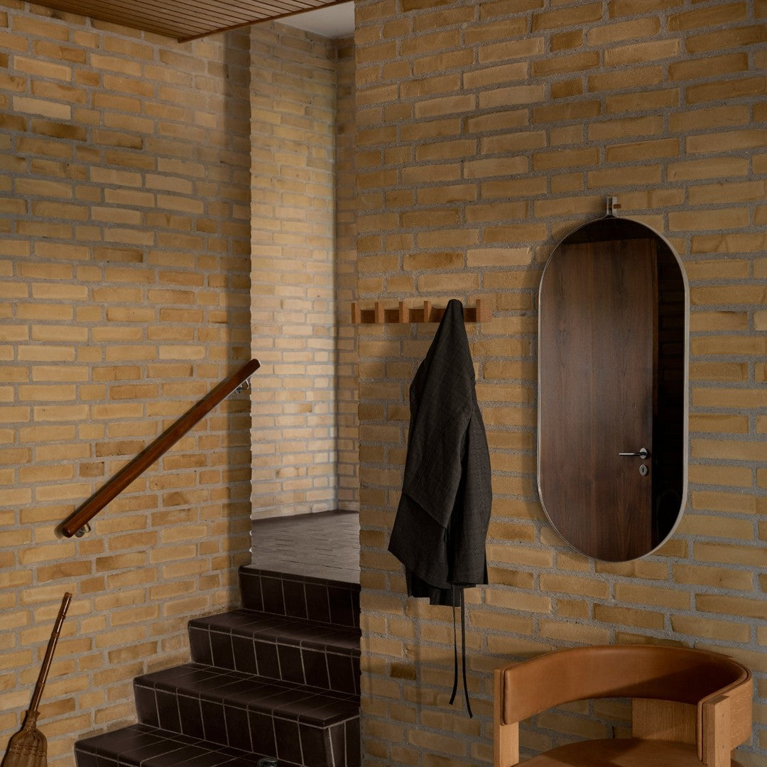 "Textured yellow brick wall with dark wooden accents; sleek, oval mirror adding a modern touch to the cozy interior."