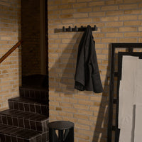 Black coat hanging on a sleek wall hook against textured beige brick and dark geometric decor.