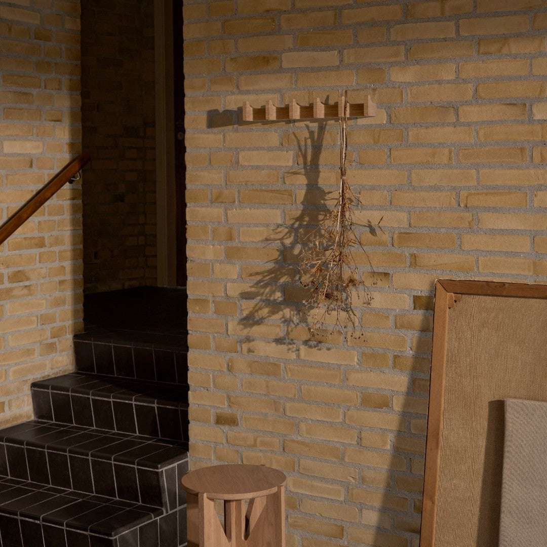 "Warm beige wall with textured bricks, dark tiled steps, and a minimalist wooden coat rack casting a shadow."