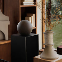 Sleek black pedestal with a round brown sculpture, showcasing minimalist design and earthy tones. Perfect for decor.