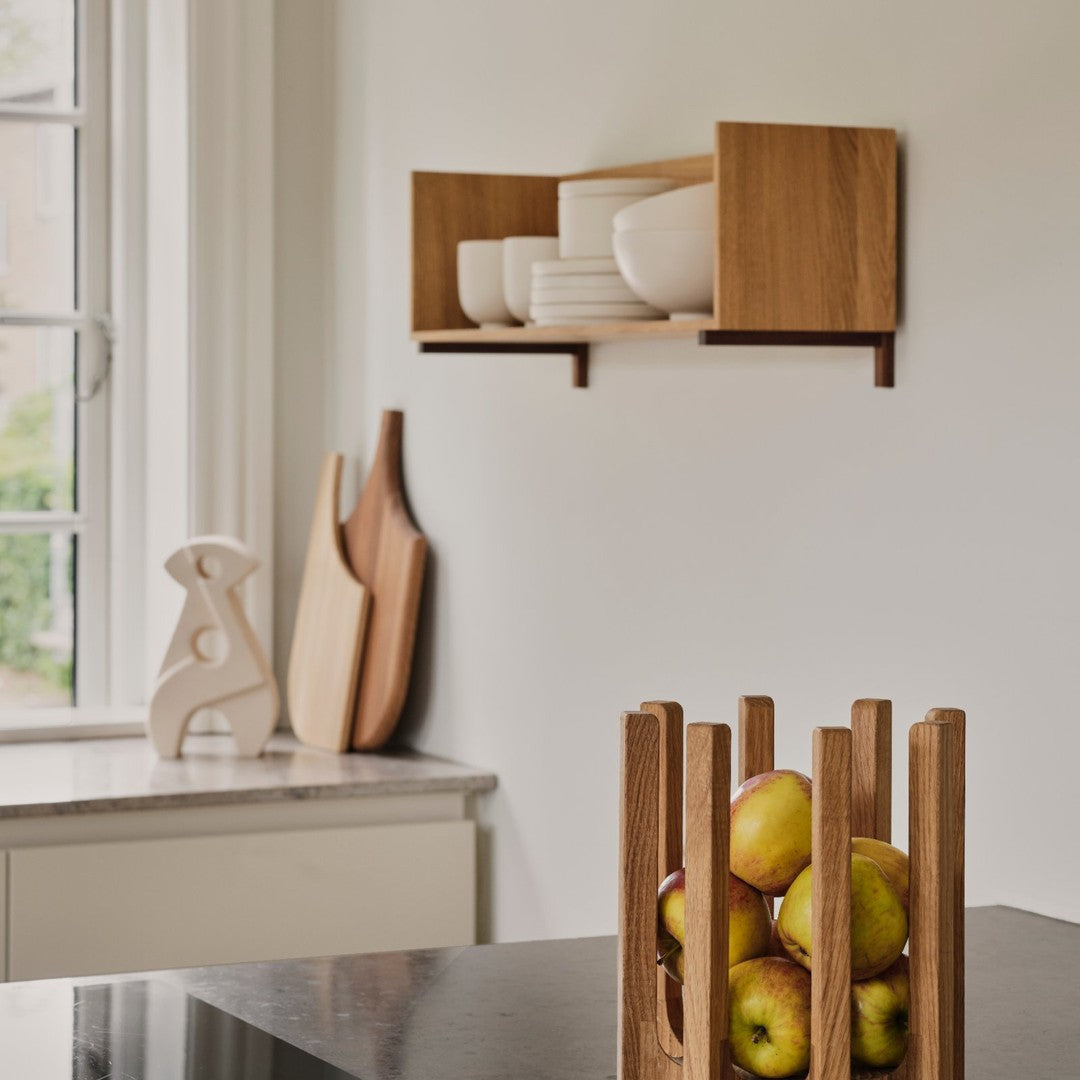"Modern wooden shelf featuring white bowls, with a natural wood fruit holder and green apples on a dark countertop."