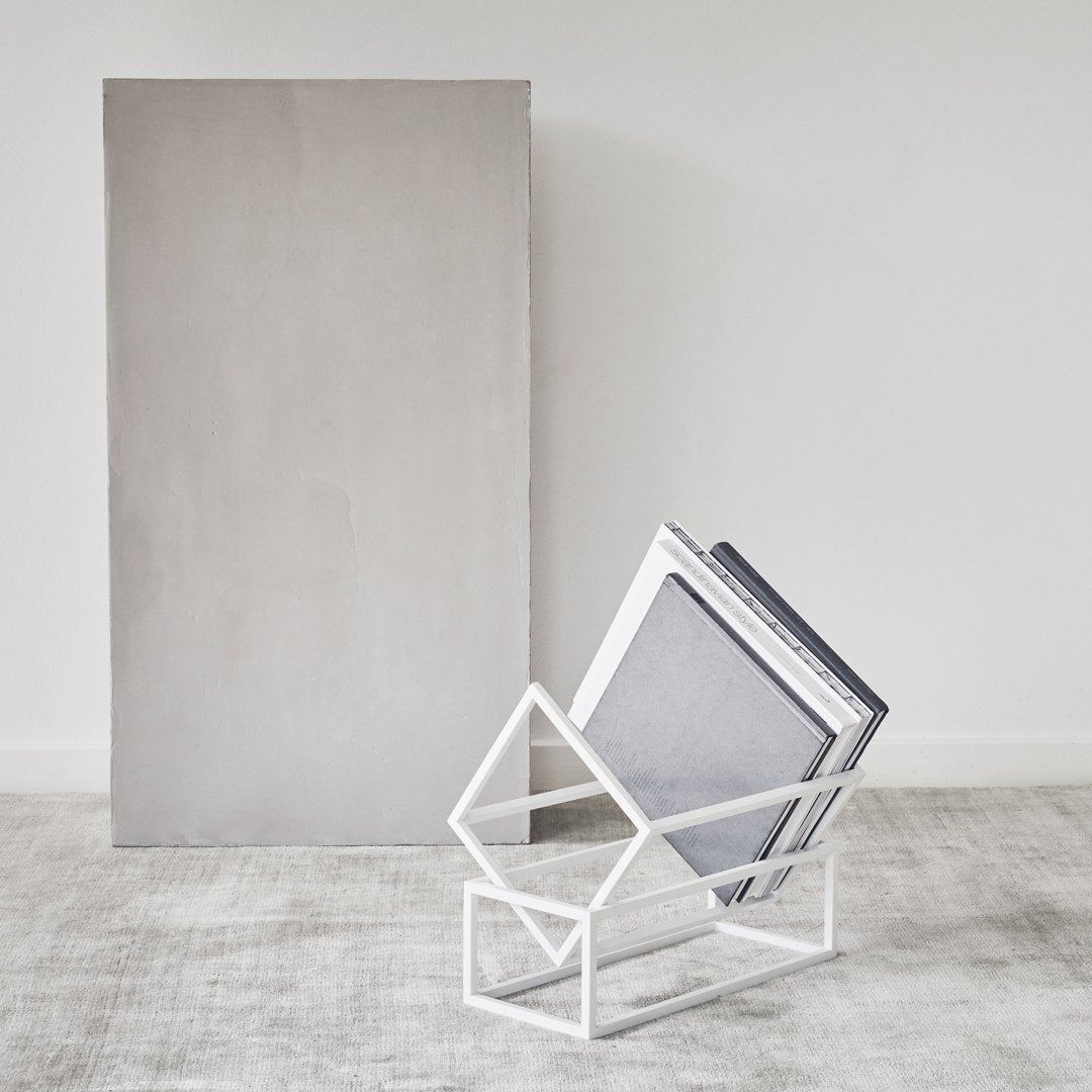 Modern white geometric magazine holder with gray books against a soft gray background, showcasing minimalistic design.