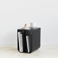 Black minimalist side table with smooth surface, showcasing a sleek design and subtle patterns.