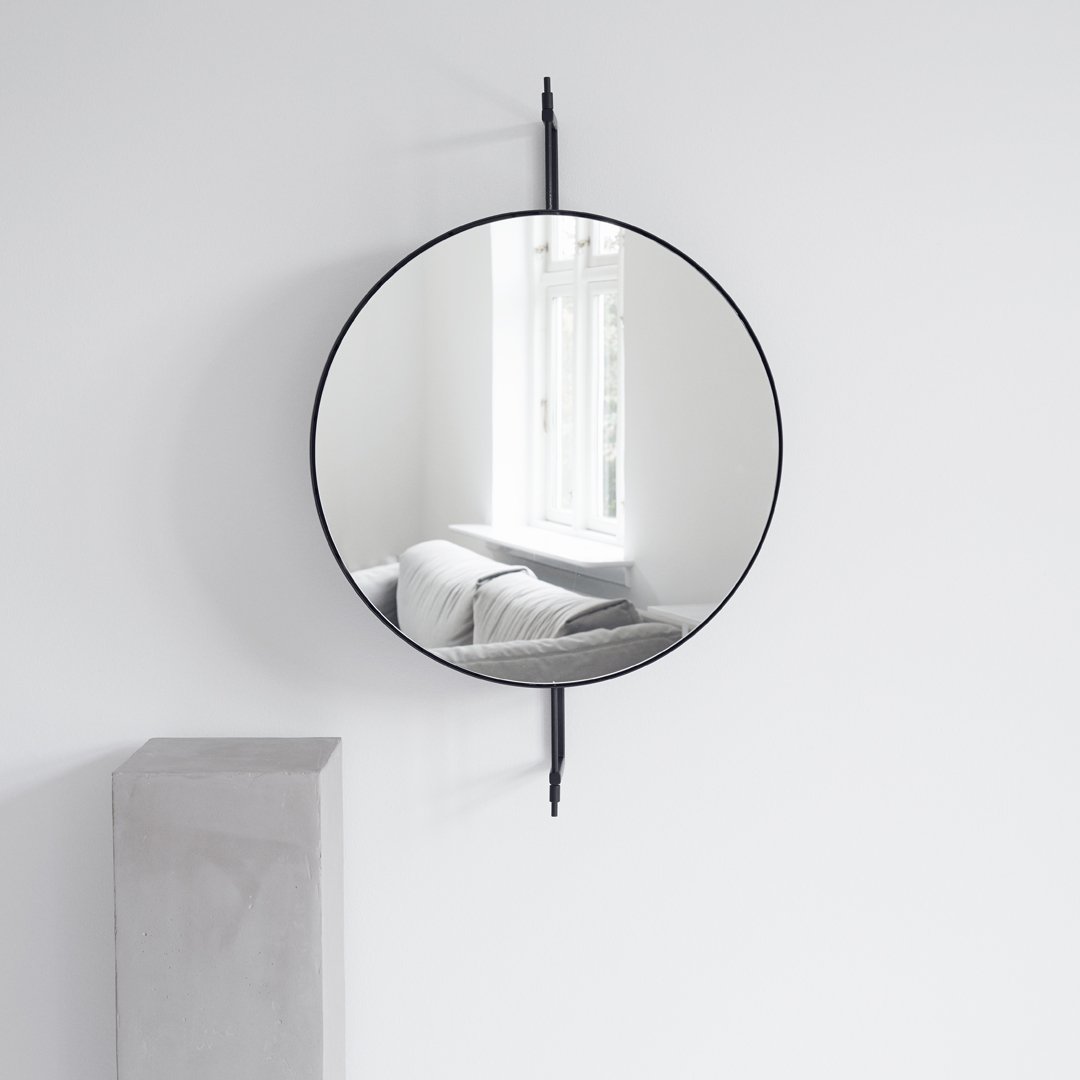 Round black-framed mirror reflecting soft gray sofa and white walls, enhancing minimalistic decor.