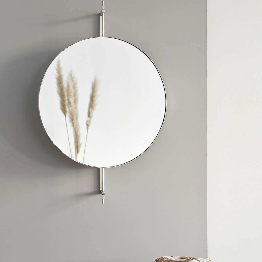 Round black-framed mirror reflecting soft gray sofa and white walls, enhancing minimalistic decor.