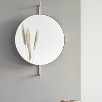 Round black-framed mirror reflecting soft gray sofa and white walls, enhancing minimalistic decor.