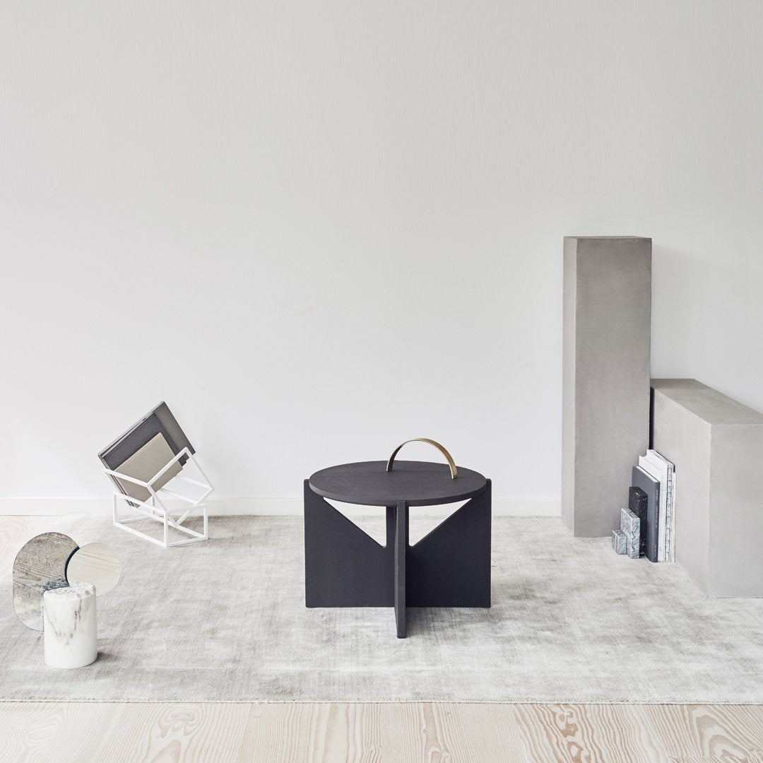 Black geometric table with a minimalist design, set against a light gray background and wood flooring.
