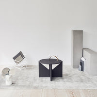 Black geometric table with a minimalist design, set against a light gray background and wood flooring.